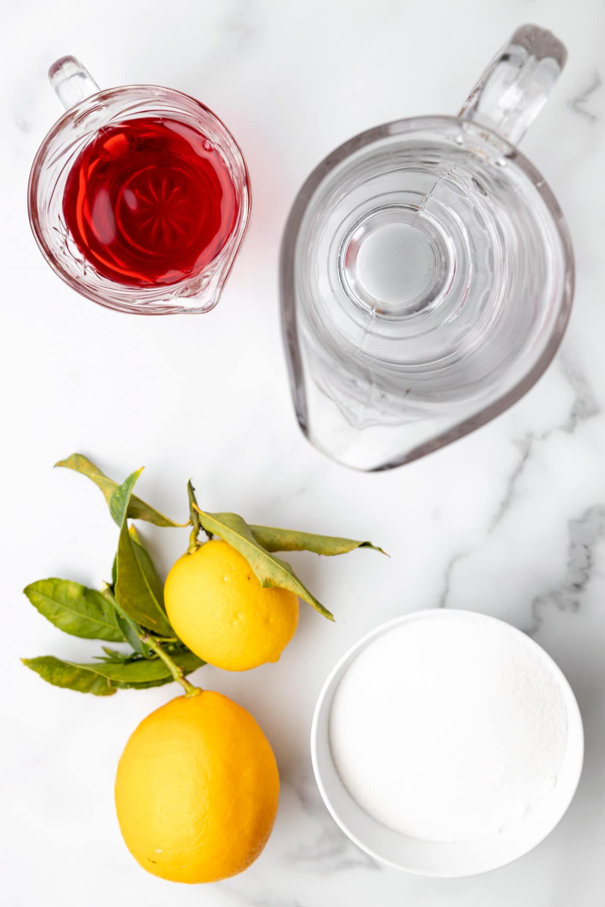 overhead view of water and cranberry juice in glass pitchers, lemons, and a bowl of sugar