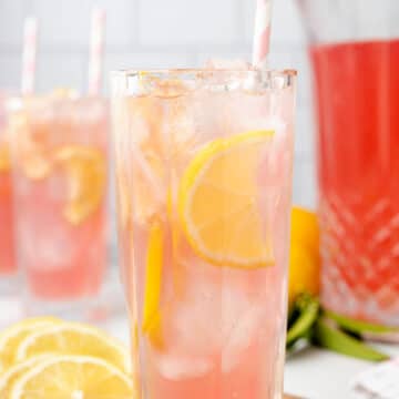 two glasses of pink lemonade with lemon slices and pink striped paper straws