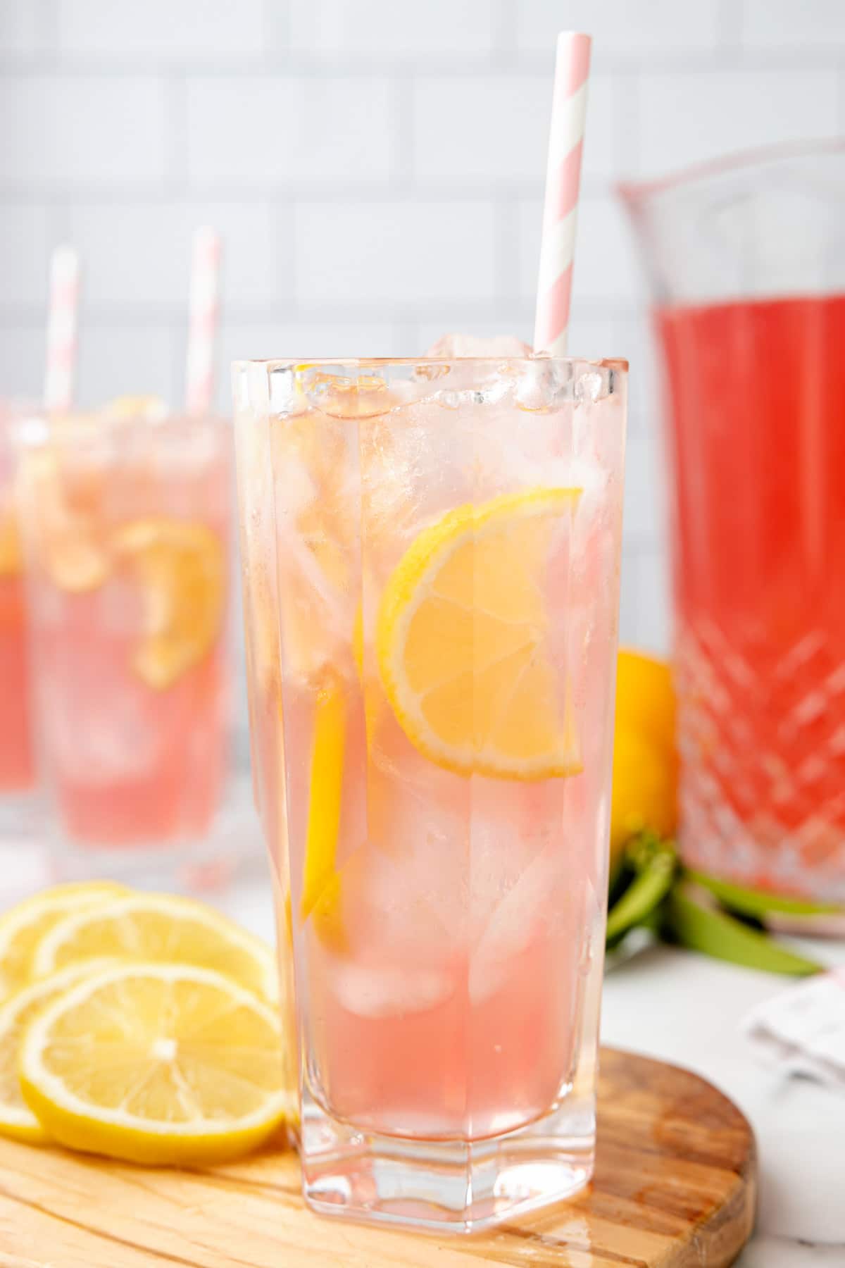 two glasses of pink lemonade with lemon slices and pink striped paper straws