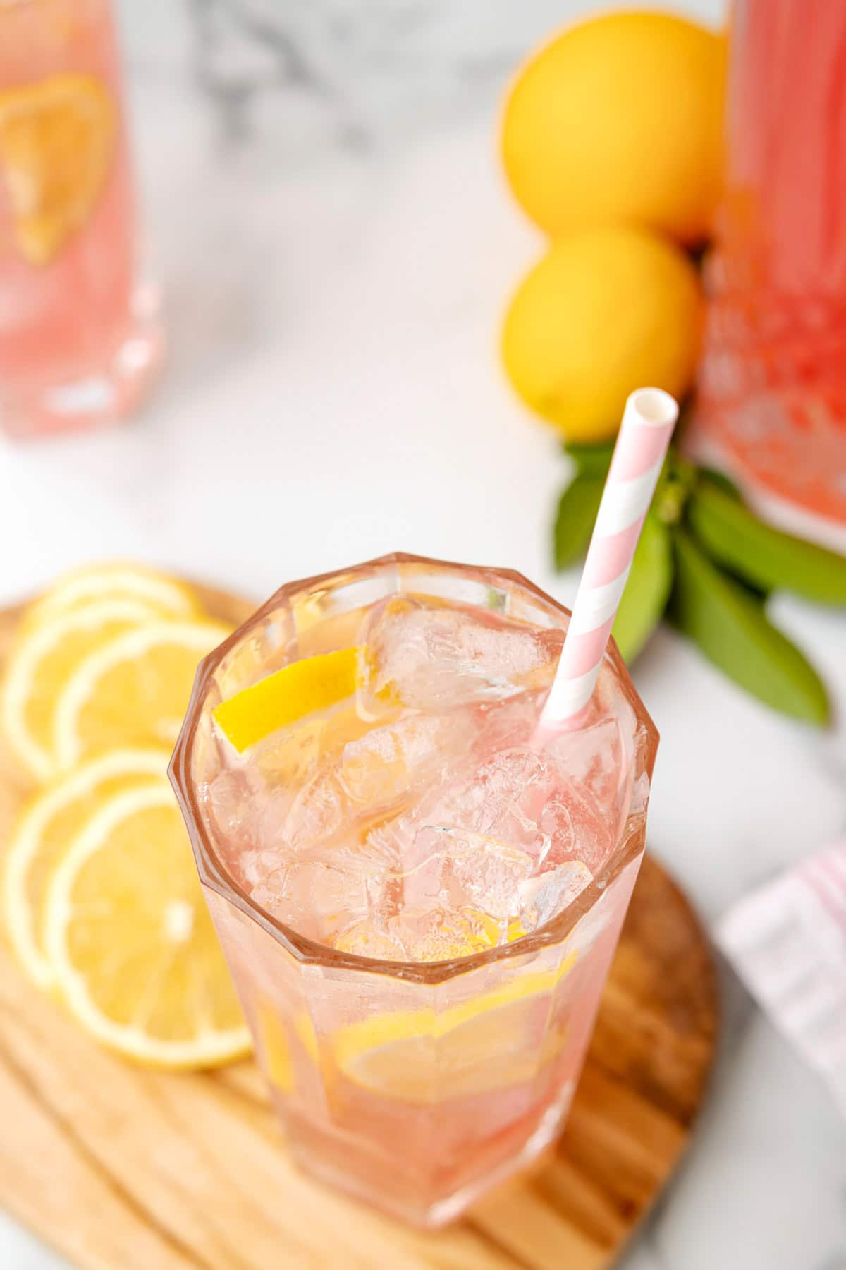 overhead photo of a glass of pink lemonade on a wood serving board with lemon slices