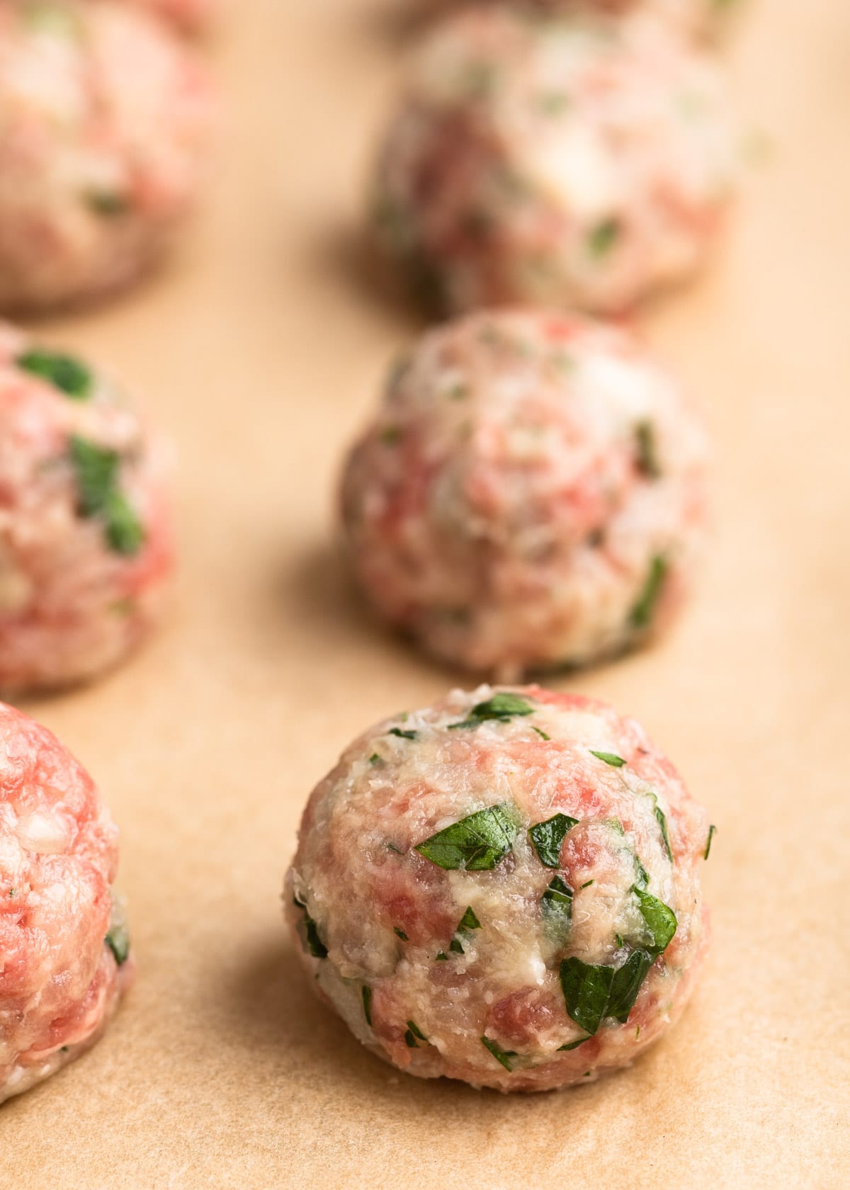 closeup view of small beef and pork meatballs on a parchment lined baking sheet