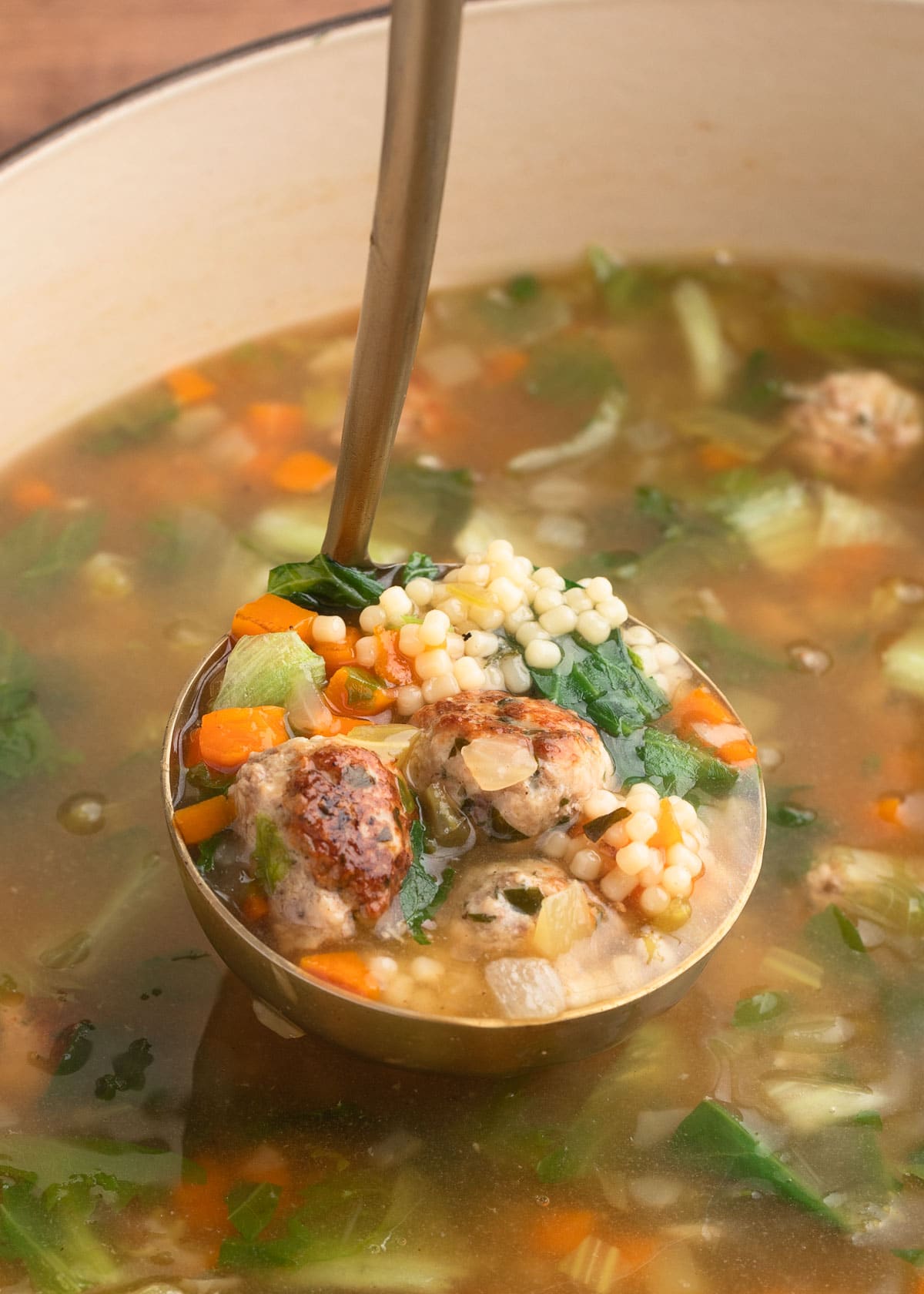 ladleful of Italian Wedding Soup in an enameled cast iron pot