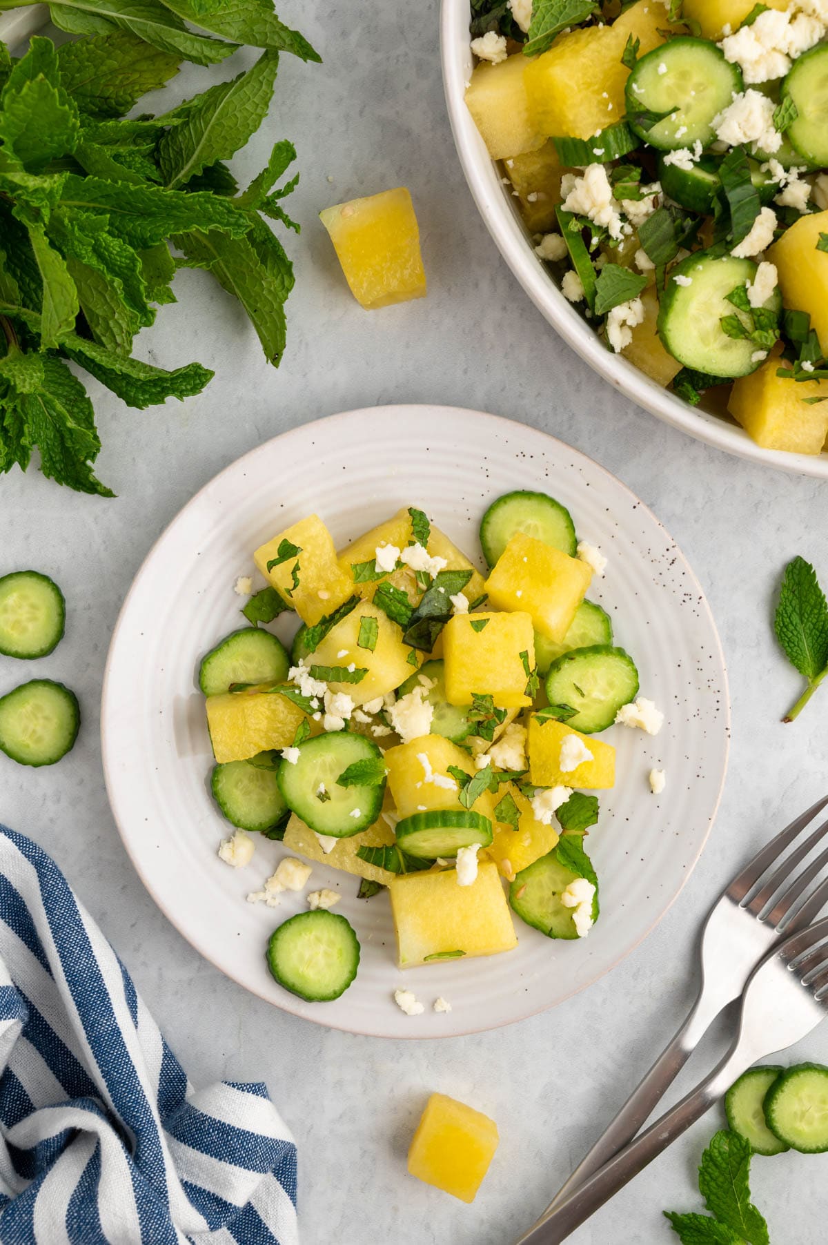 overhead photo of watermelon feta salad served on a white plate next to 2 forks and a blue and white striped napkin