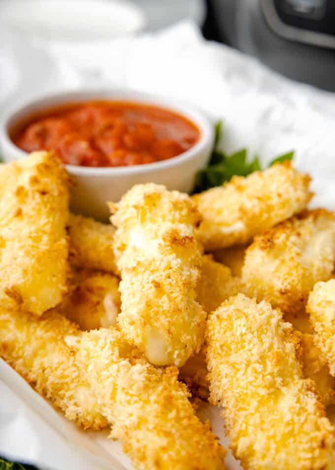 air fried mozzarella sticks on a parchment-lined platter with a bowl of marinara sauce