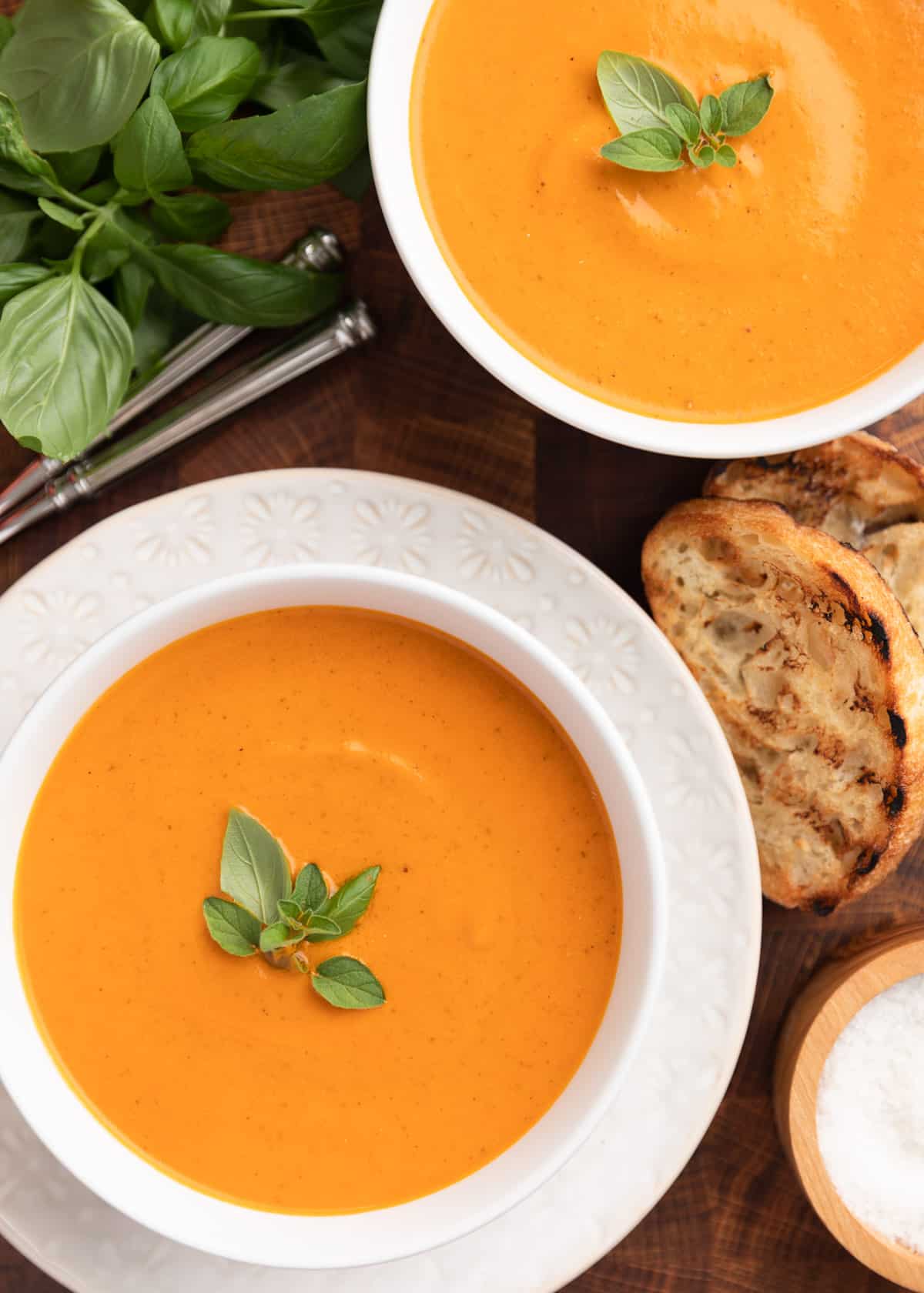 overhead photo of two bowls of creamy roasted tomato soup on a wood board