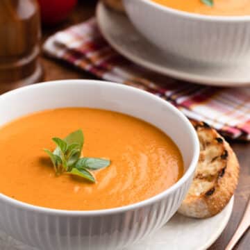 two white porcelain bowls of creamy roasted tomato soup with fresh basil garnish