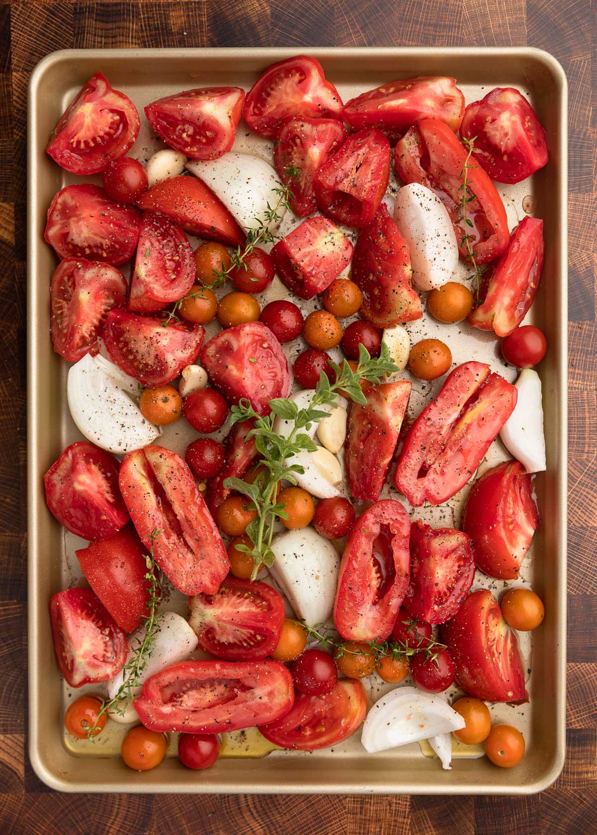 overhead photo of tomatoes, onions, garlic, and herbs on a baking sheet