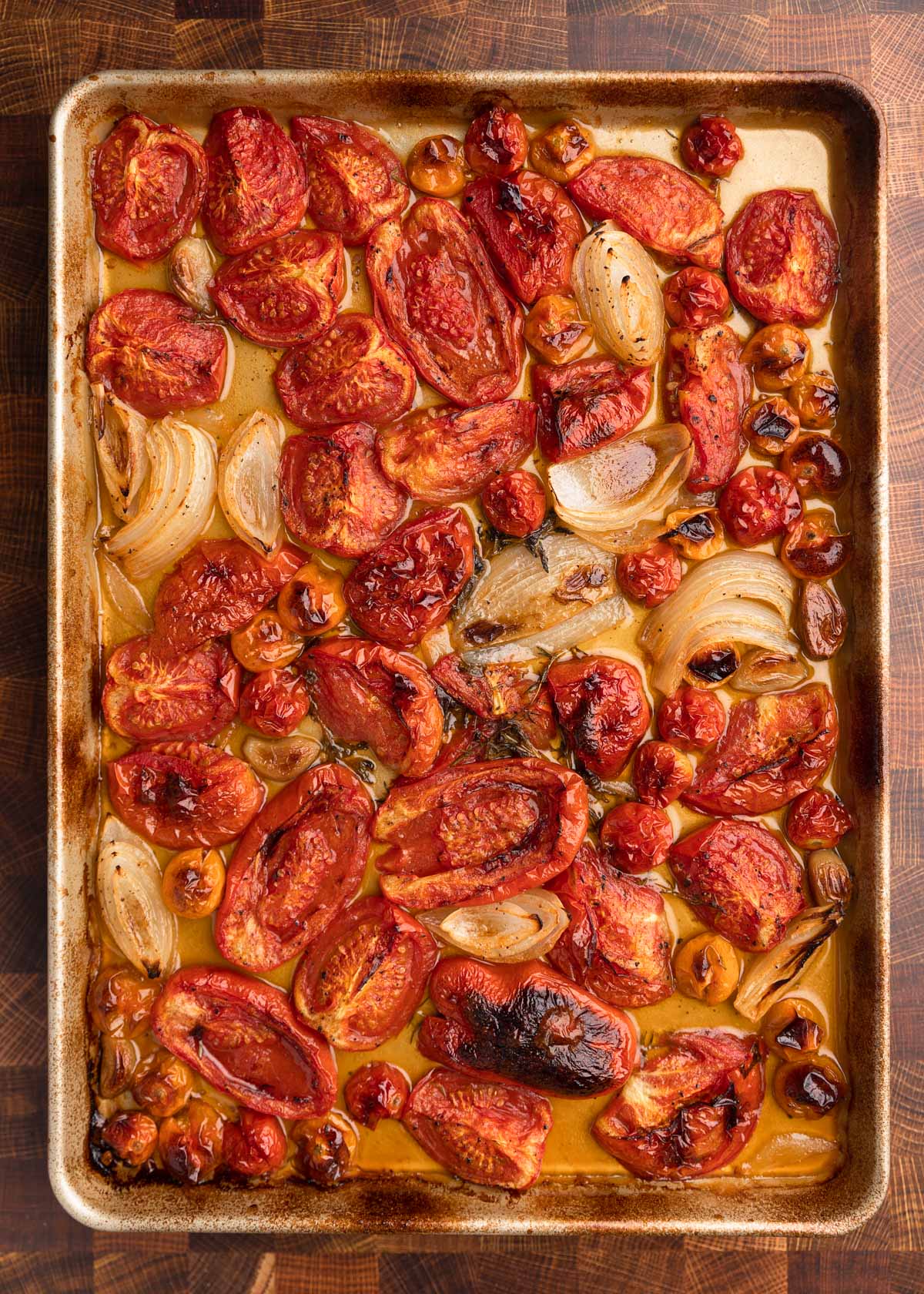 overhead photo of roasted tomatoes, garlic cloves, and onions on a sheet pan