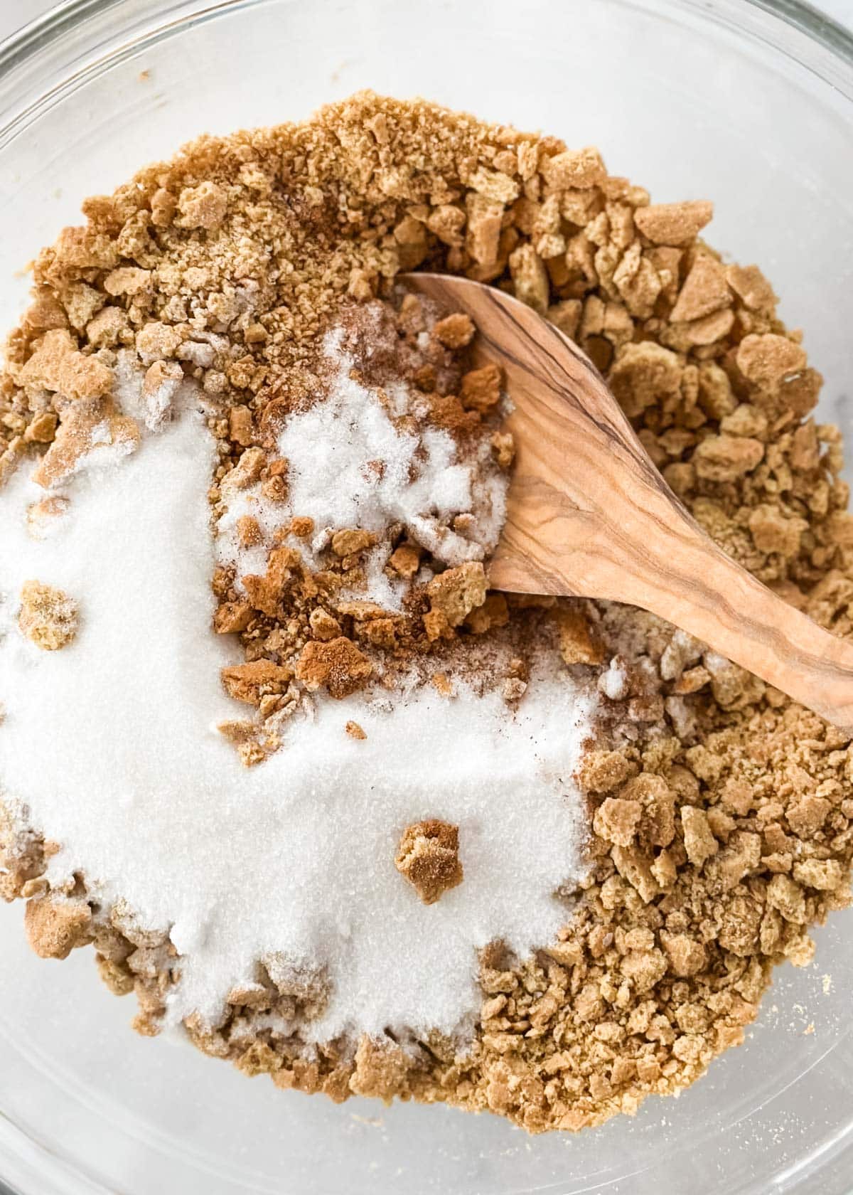 closeup of graham cracker crumbs, sugar, and cinnamon in a glass bowl with a wooden spoon