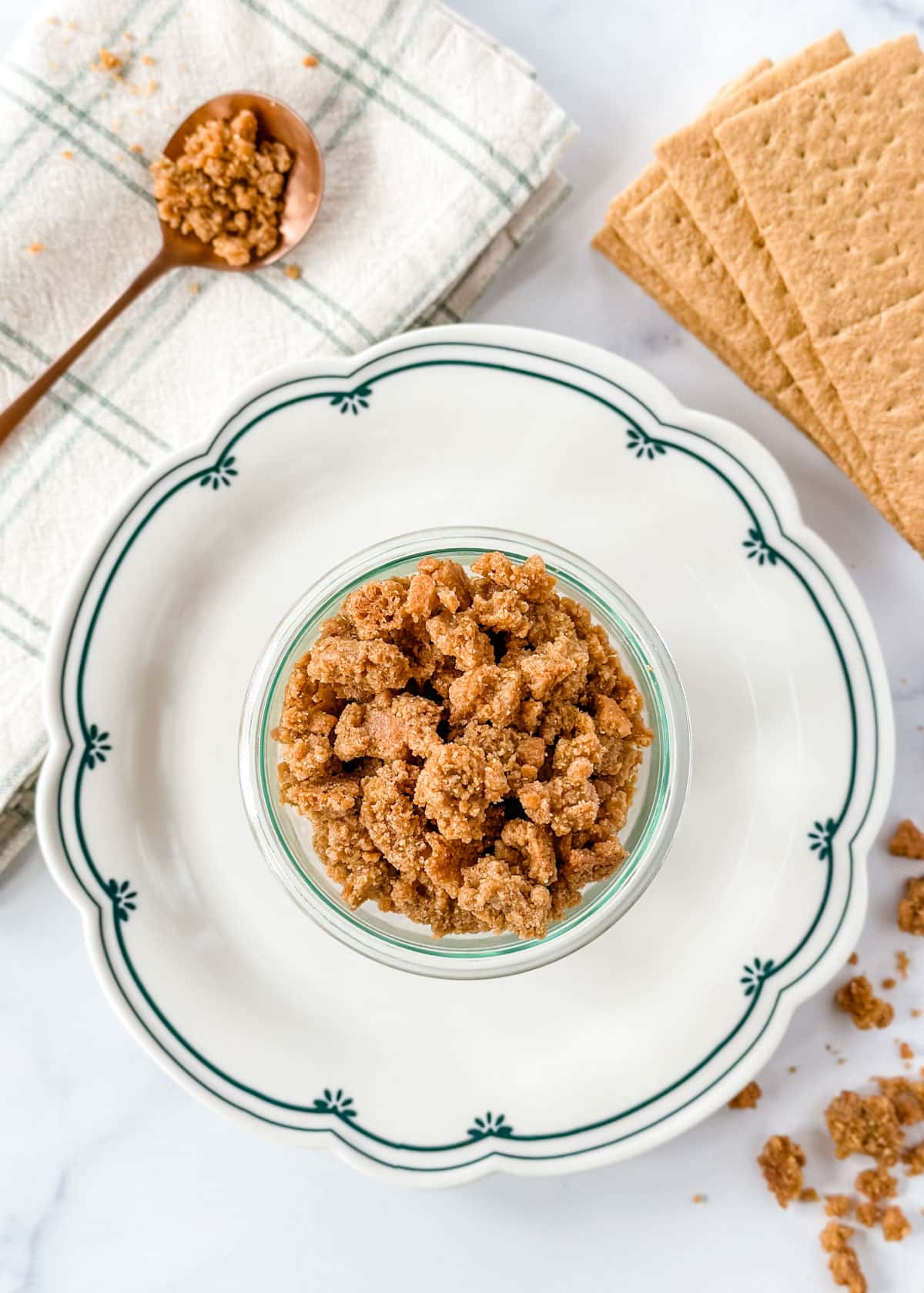 overhead photo of graham cracker crumbles in a glass jar on a blue and white scalloped plate