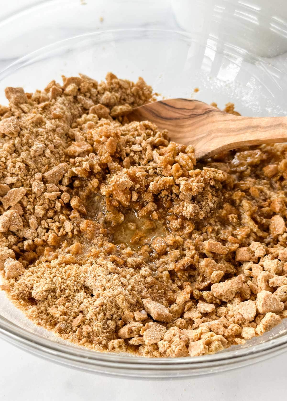 crushed graham crackers, sugar, and melted butter in a glass bowl with a wooden spoon