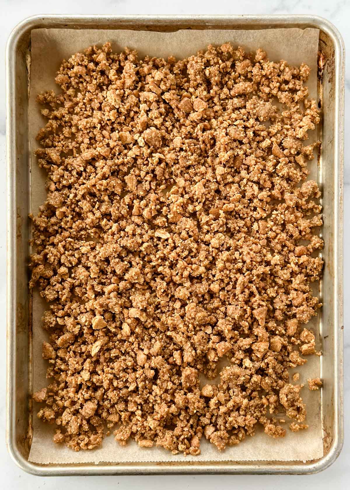 unbaked graham cracker crumbles on a parchment-lined baking sheet