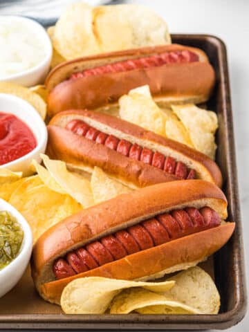 air fryer hot dogs on a baking sheet with potato chips and bowls of relish, ketchup, and chopped onions