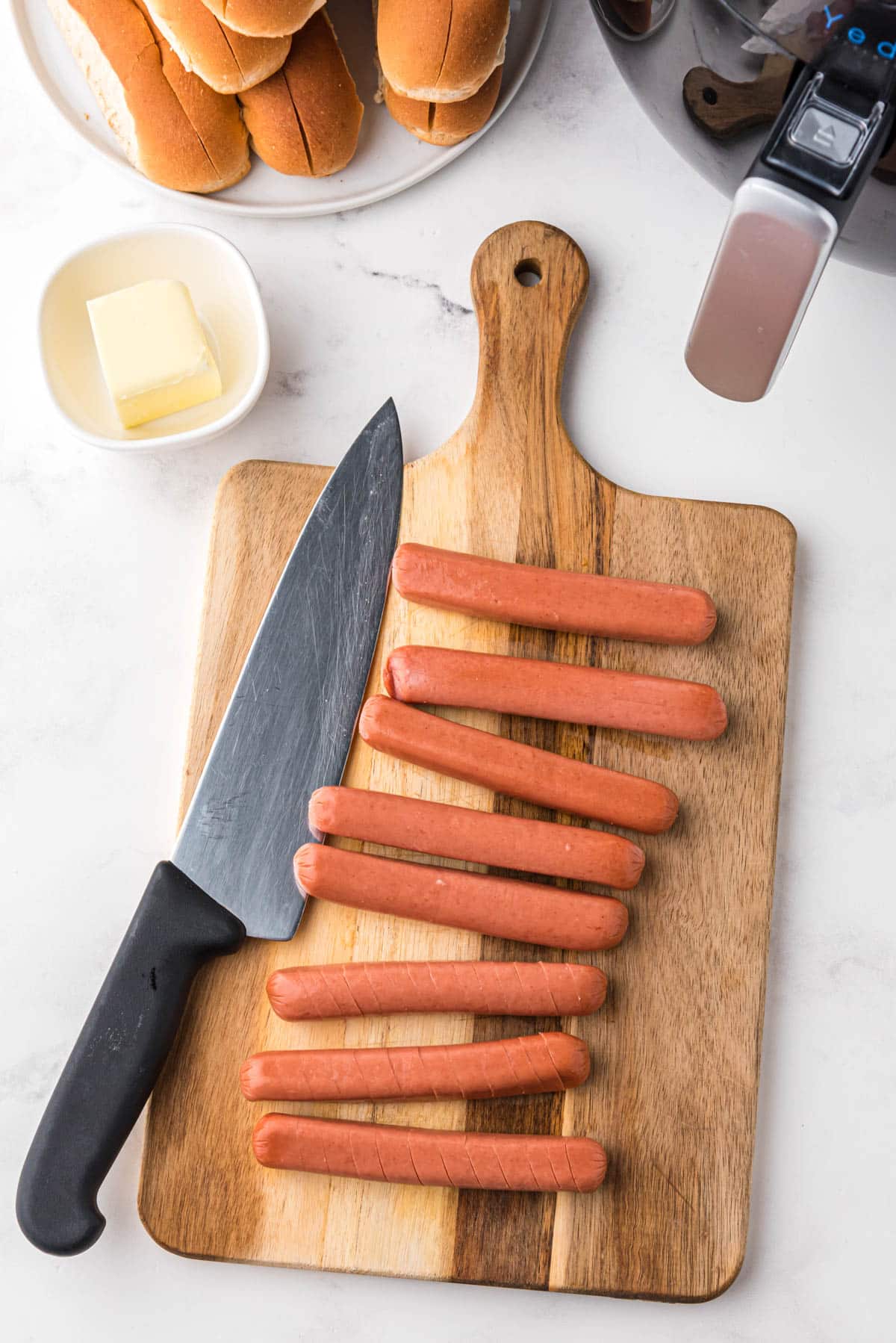 overhead photo of hot dogs on a wooden board with a chef's knife