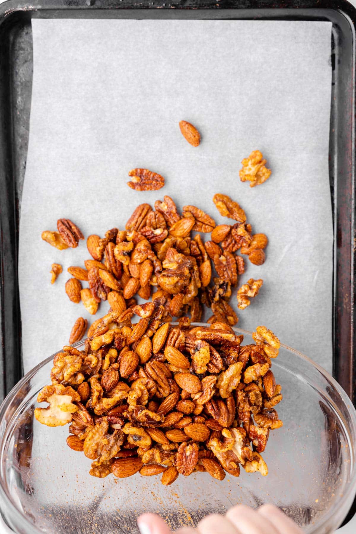 overhead photo showing spicy nut mix being poured onto a parchment-lined baking sheet