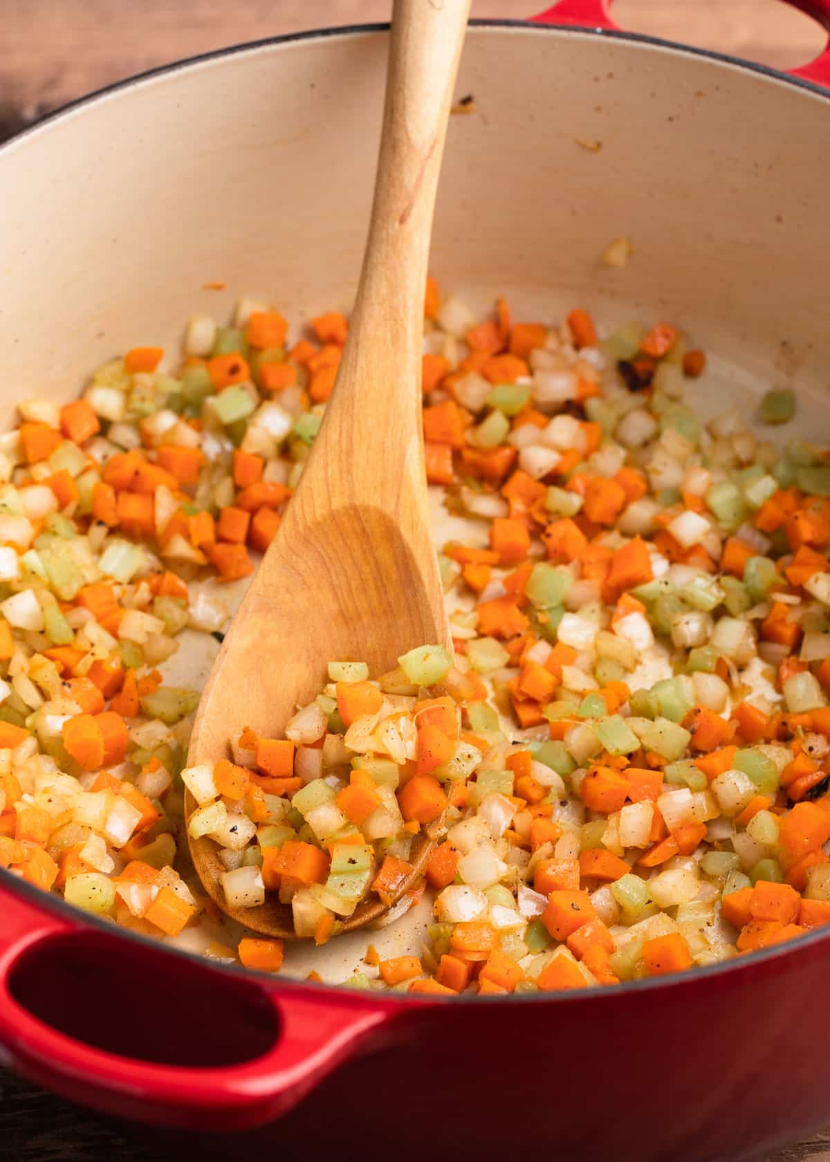 sautéed celery, carrots, and onions in an enameled cast iron Dutch oven with a wooden spoon 