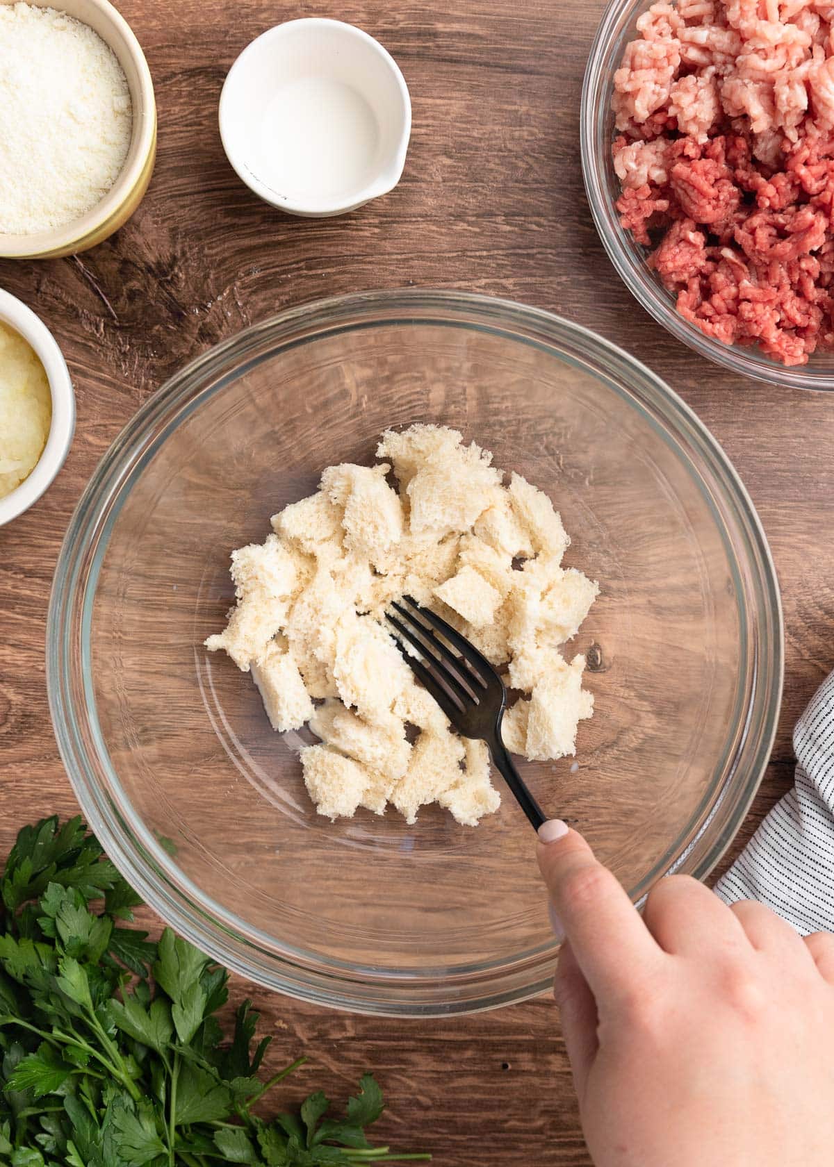 milk soaked white bread in a glass bowl being mashed with a black fork
