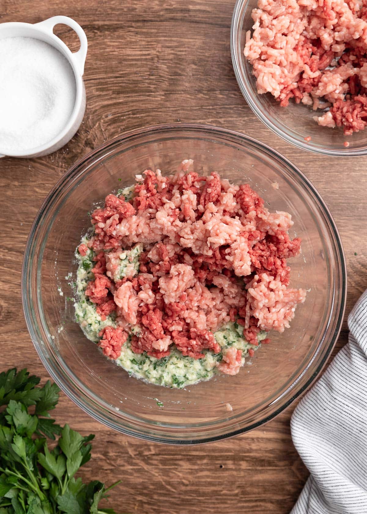 ground beef and pork in a glass bowl with a seasoned panade on a wood board