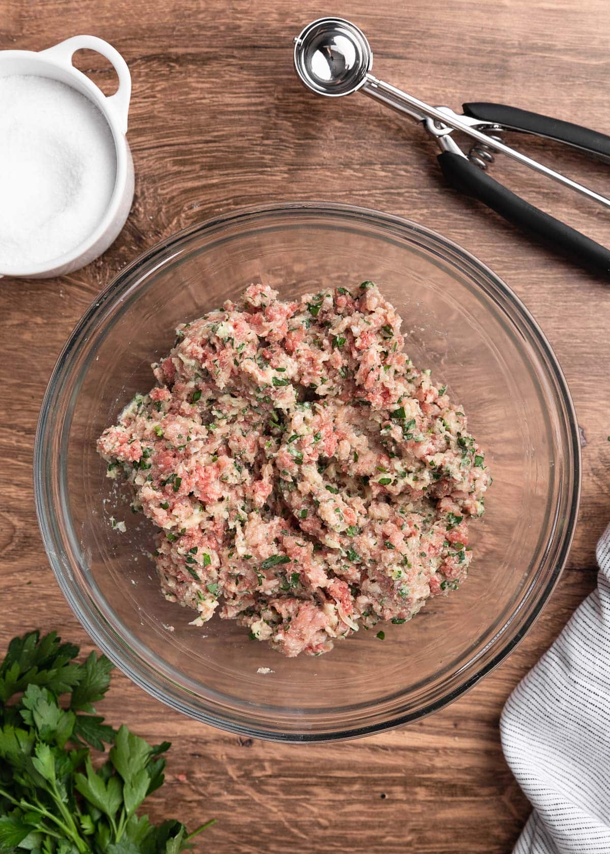 uncooked meatball mixture in a glass bowl on a wood board