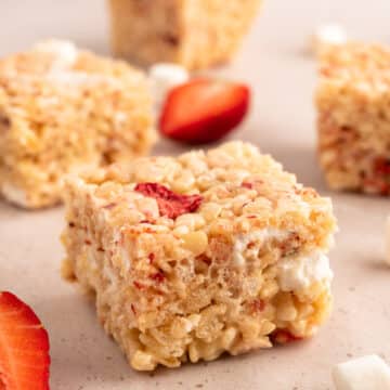 cut strawberry rice krispie treat squares on a beige background with strawberry wedges and miniature marshmallows
