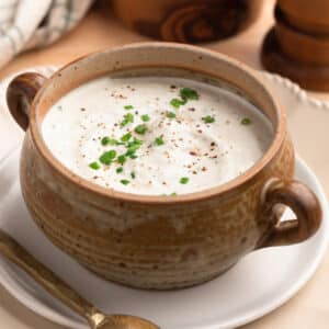 creamy horseradish sauce with chives in a tan ceramic crock