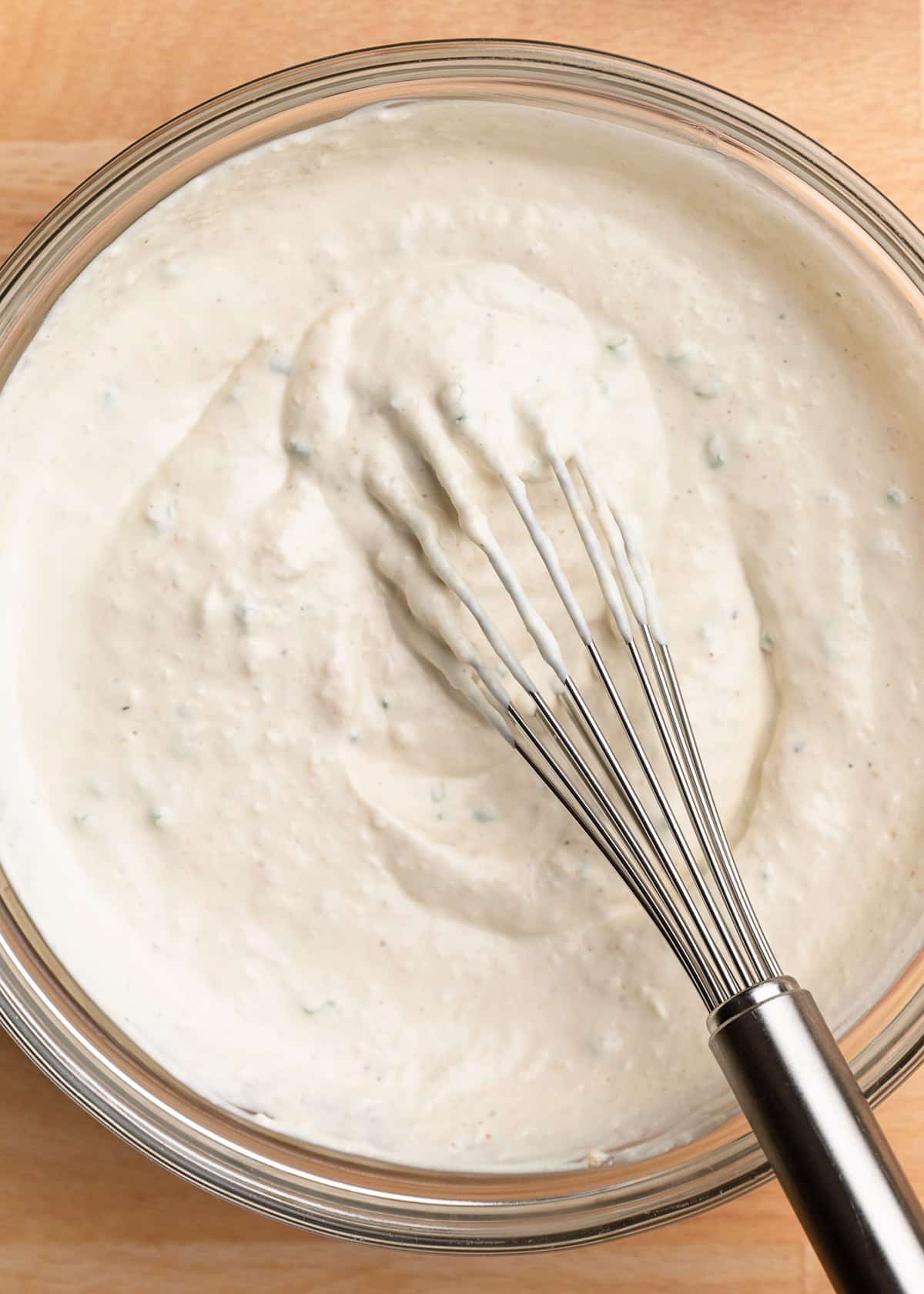 closeup overhead photo of horseradish cream sauce being mixed in a glass bowl with a stainless steel whisk