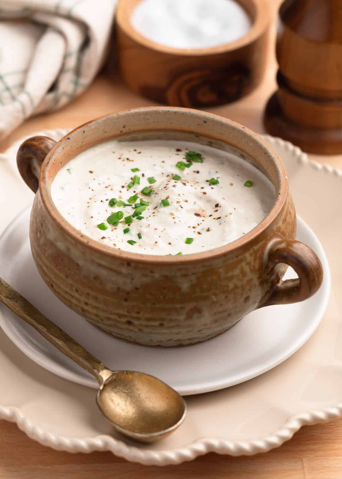 creamy horseradish sauce in a tan ceramic crock on a small white plate with a brass spoon