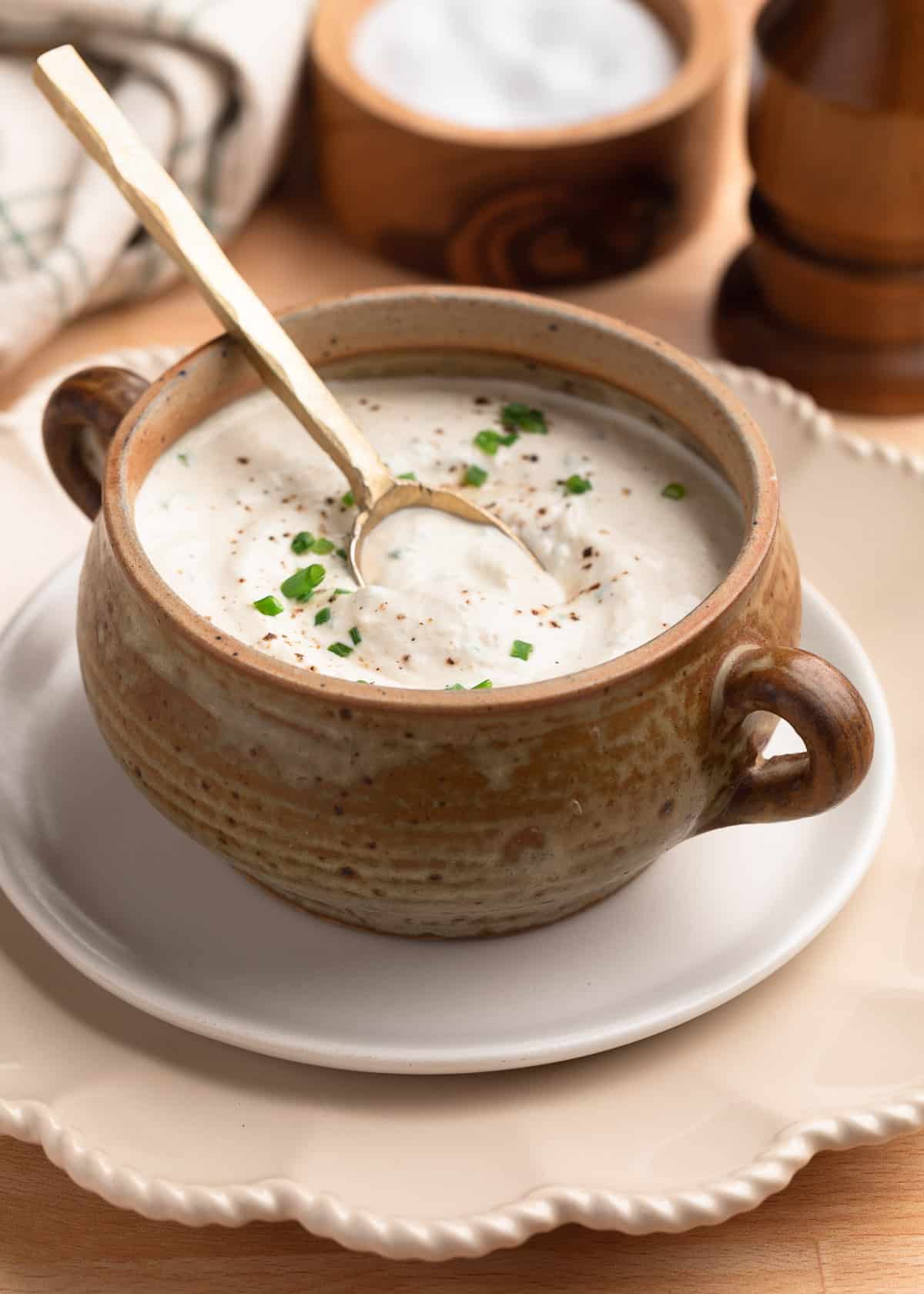 creamy horseradish sauce in a tan crock on a white plate with a brass spoon dipped into the sauce