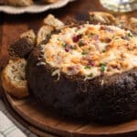 Reuben Dip in a Pumpernickel Bread Bowl on a wooden plate, surrounded by rye and pumpernickel toast dippers