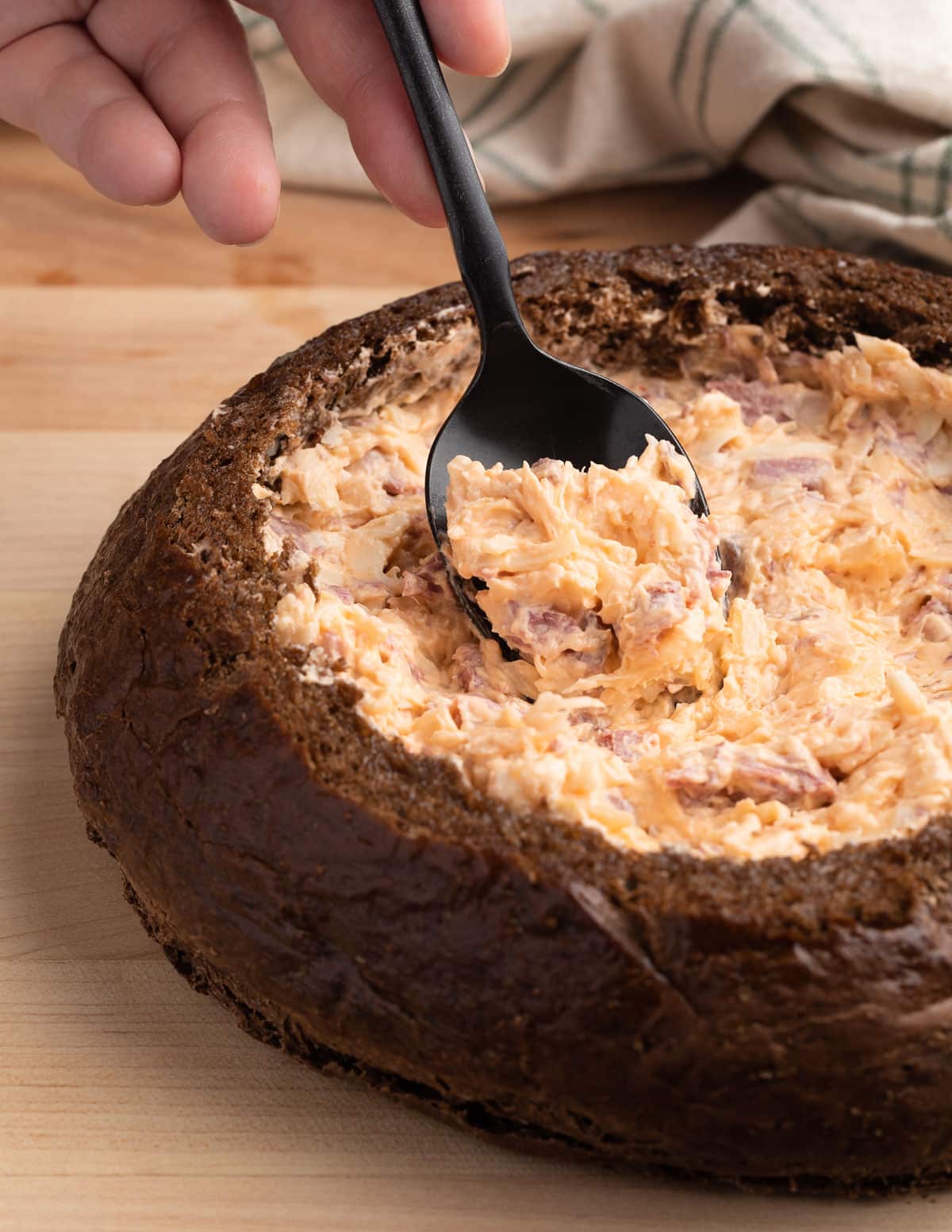 reuben dip being spooned into a pumpernickel bread bowl with a black spoon