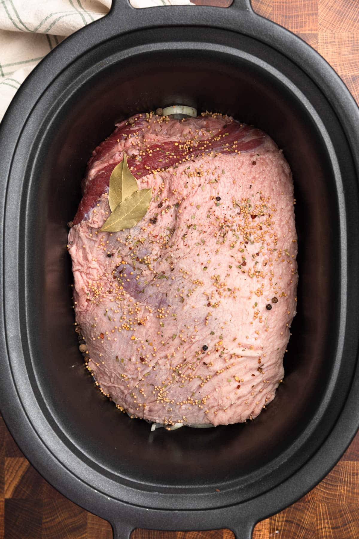 uncooked corned beef brisket with spices in a black slow cooker insert