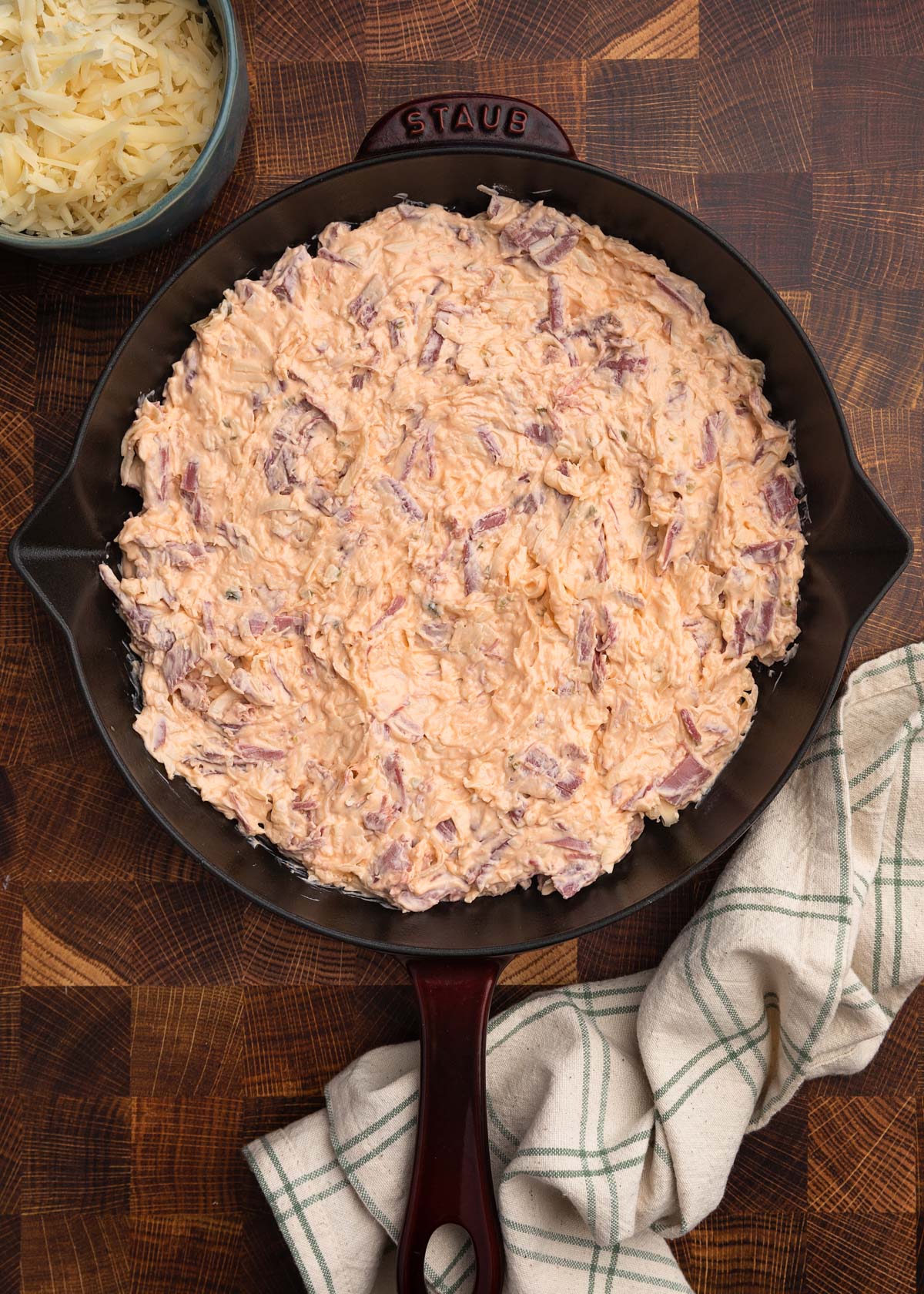 overhead photo of unbaked reuben dip in a staub cast iron skillet on a butcher block board