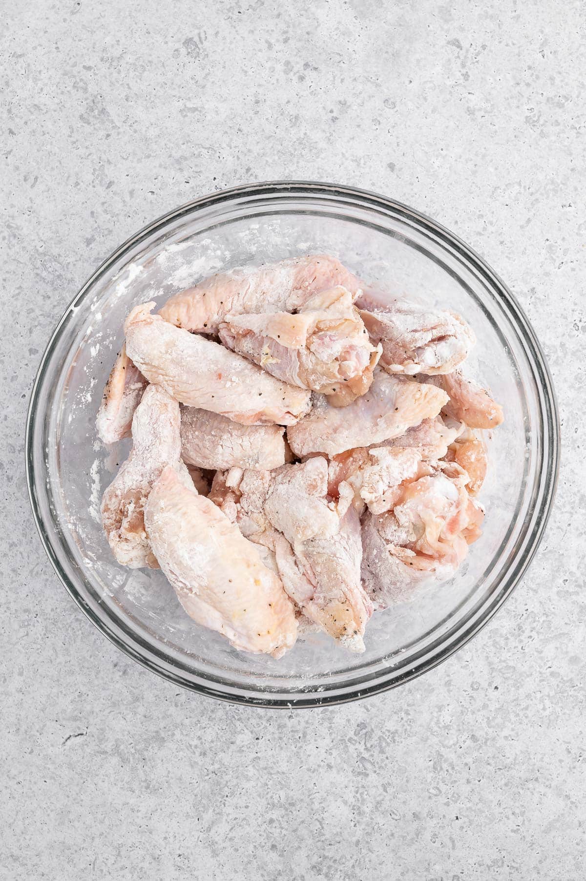 raw chicken wings in a glass bowl coated with cornstarch and seasonings