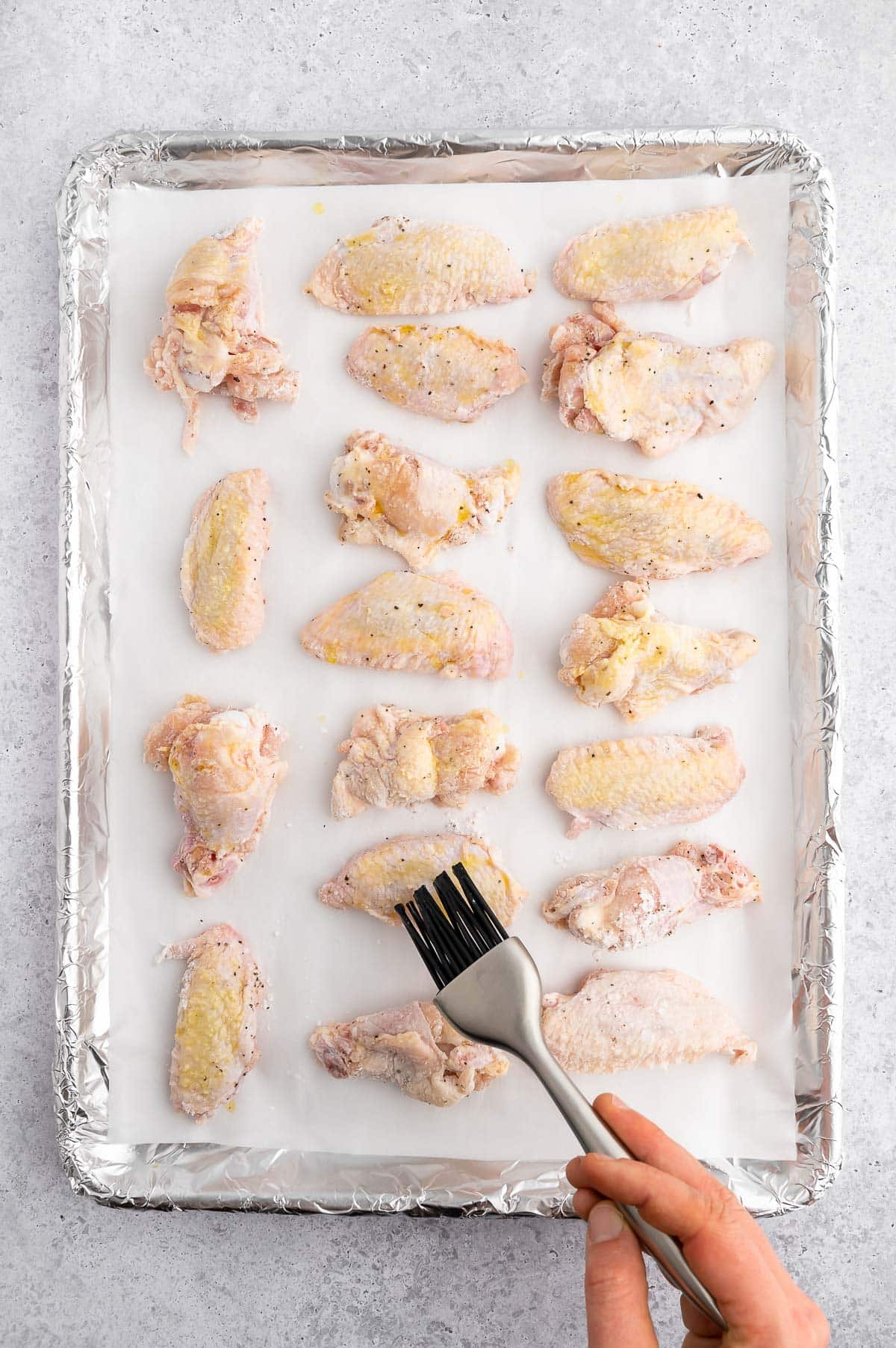 brushing raw chicken wings on a lined sheet pan with oil