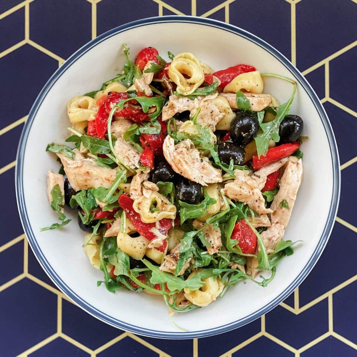 chicken tortellini salad in a white bowl on a yellow and blue geometric background