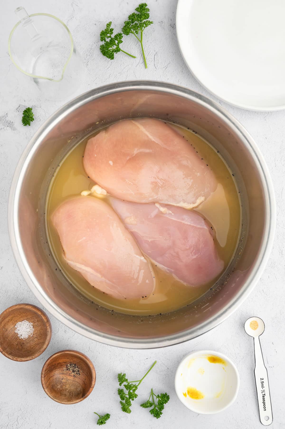 overhead photo of raw chicken breasts sitting in seasoned chicken bouillon in a stainless steel Instant Pot insert