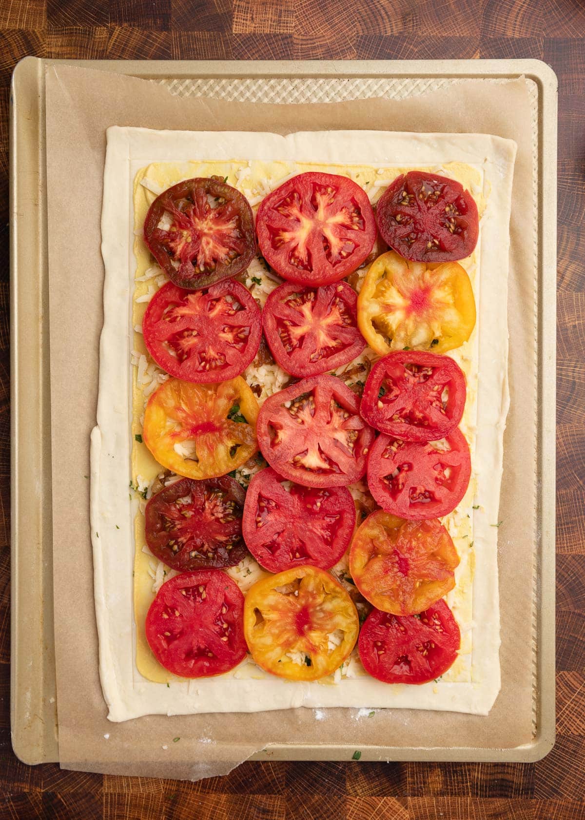 overhead photo of an unbaked puff pastry tomato tart on a parchment lined baking sheet