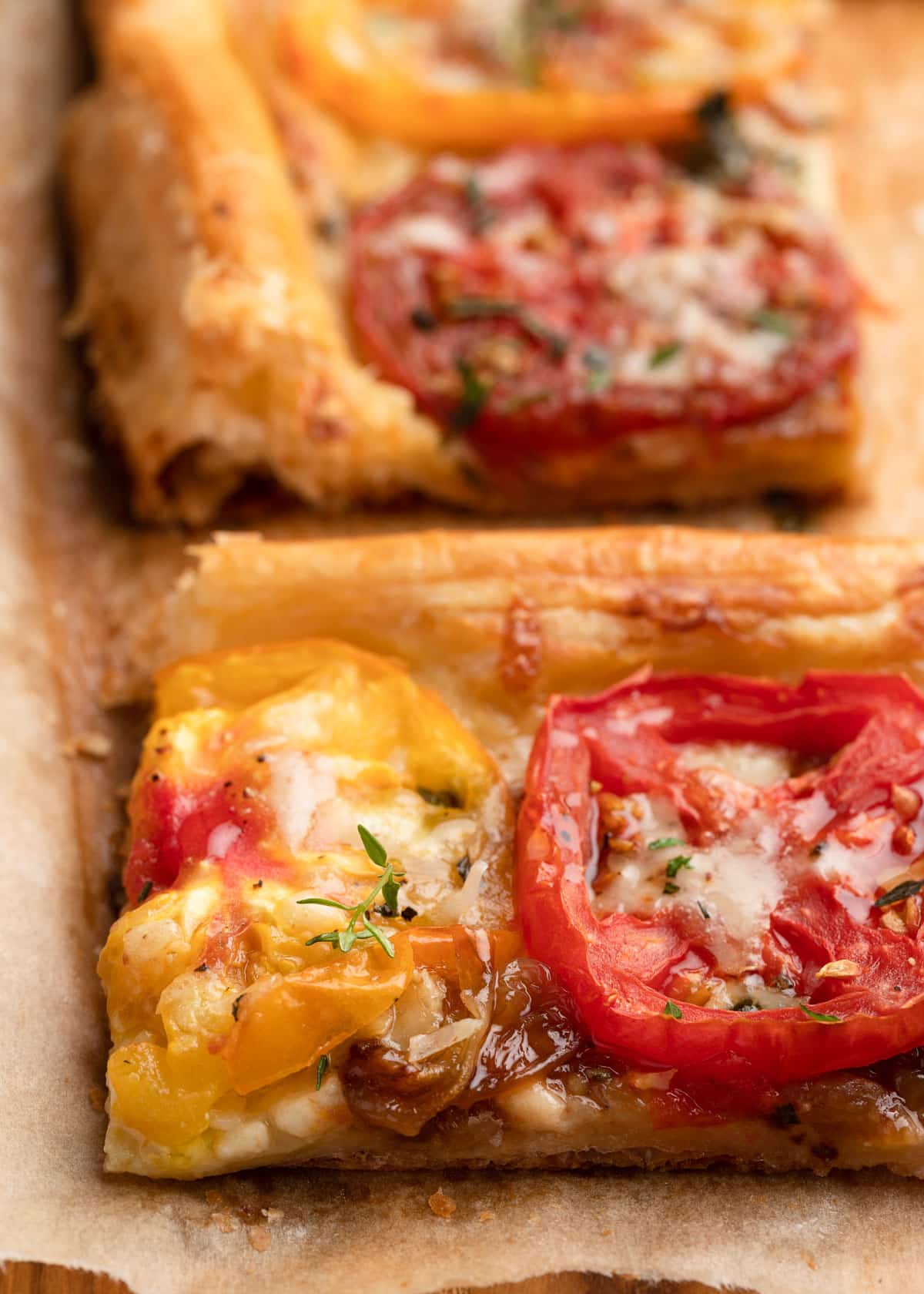 closeup of a slice of baked puff pastry tomato tart on parchment paper