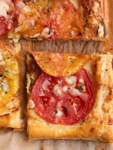 closeup of a sliced puff pastry tomato tart on parchment paper
