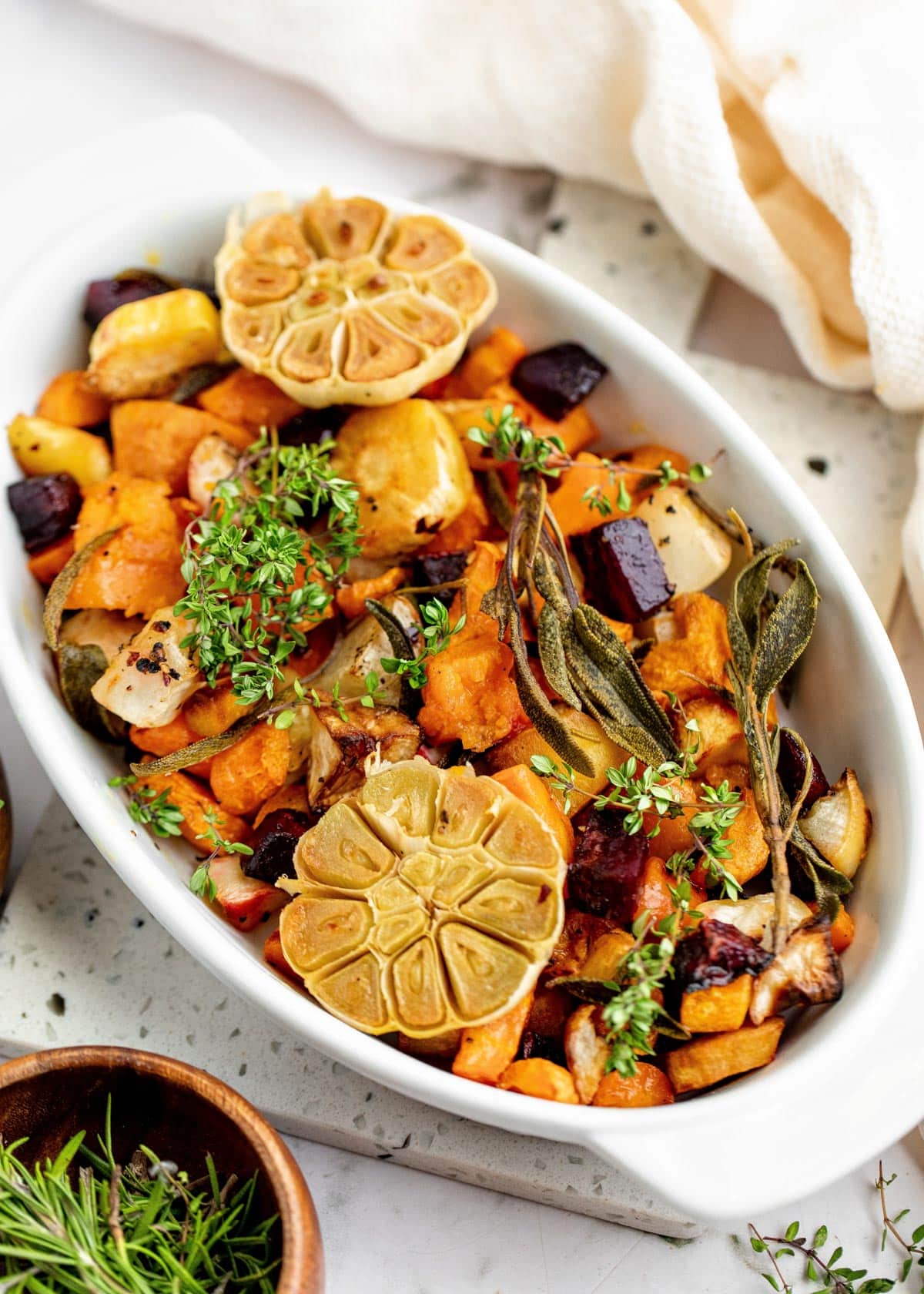 roasted assorted root vegetables in a white gratin dish garnished with fresh herbs