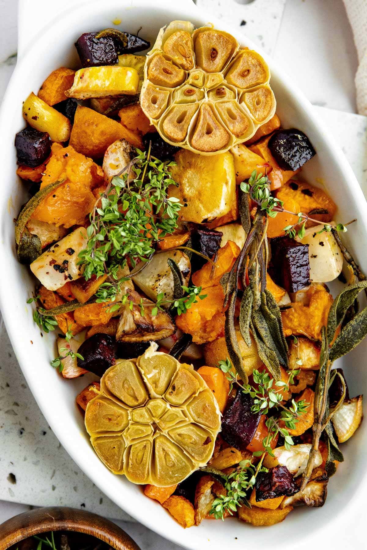 overhead photo of roasted root vegetables in a white gratin dish, garnished with fresh herbs