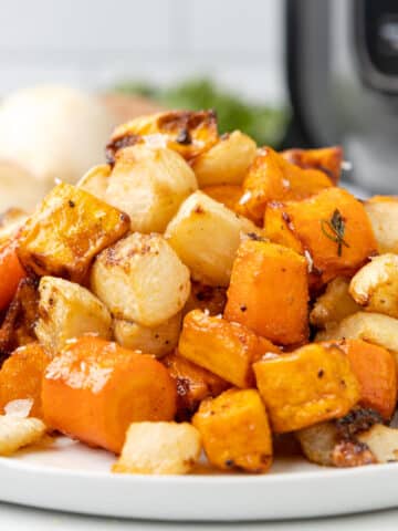 closeup of air fryer roasted carrots, turnips, and sweet potatoes on a white plate with an air fryer in the background