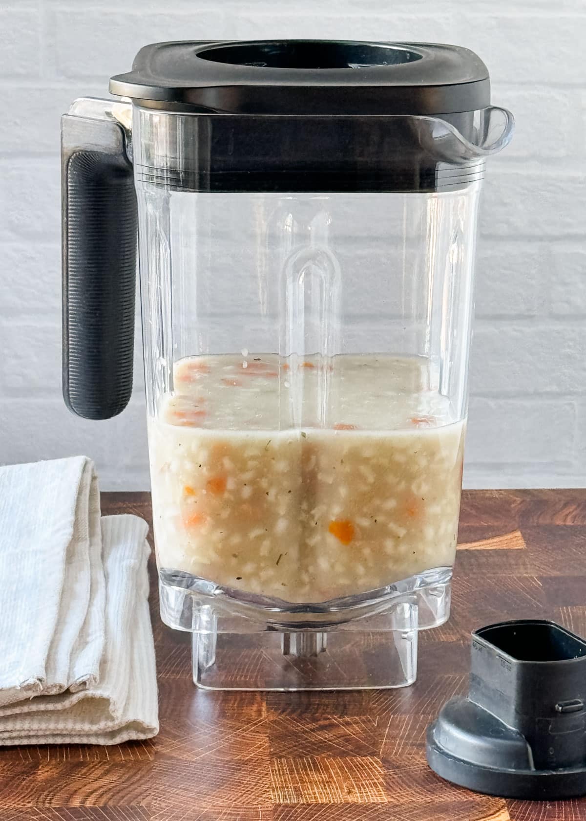 blender jar filled halfway with chicken rice soup on a butcher block counter