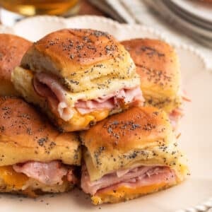 baked ham and cheese sliders on a double stack of ivory ceramic plates, with a glass of beer in the background