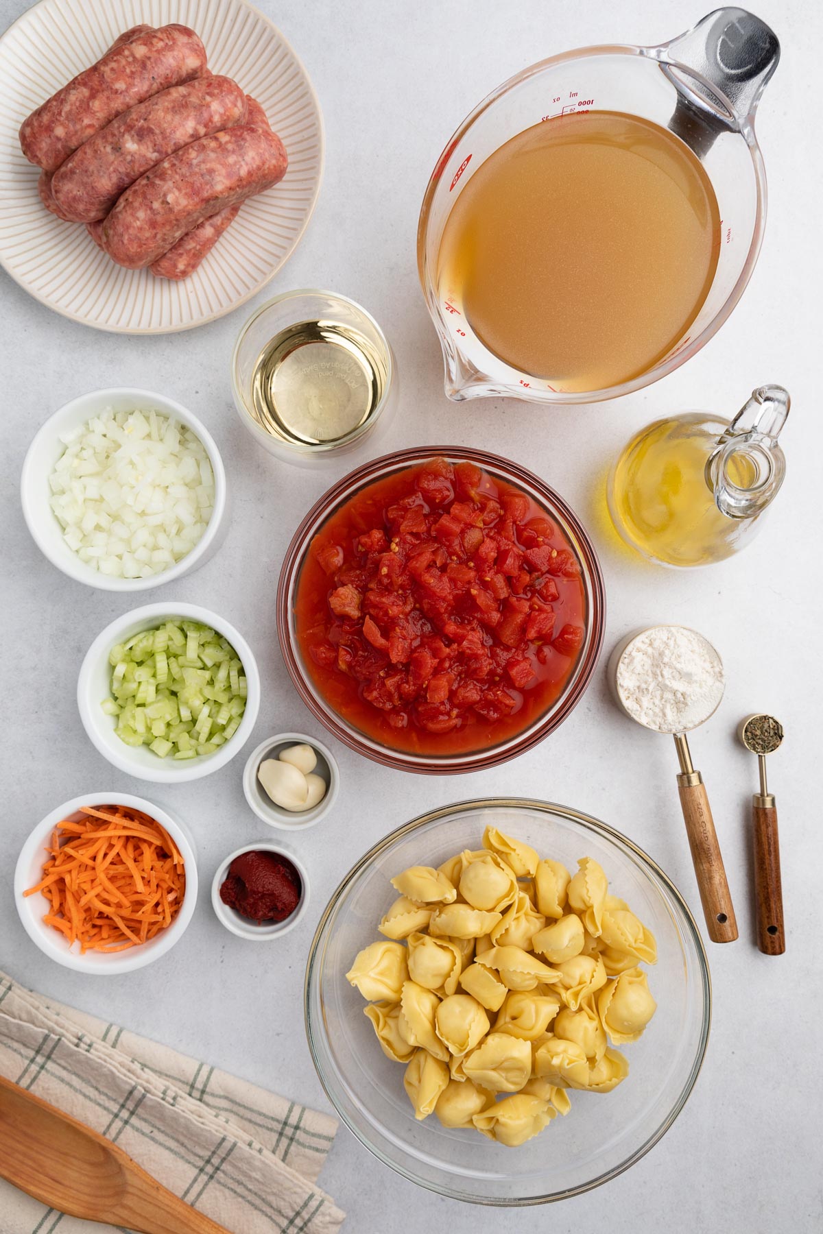 overhead photo showing prepped ingredients for tortellini sausage soup in bowls and plates on a white background