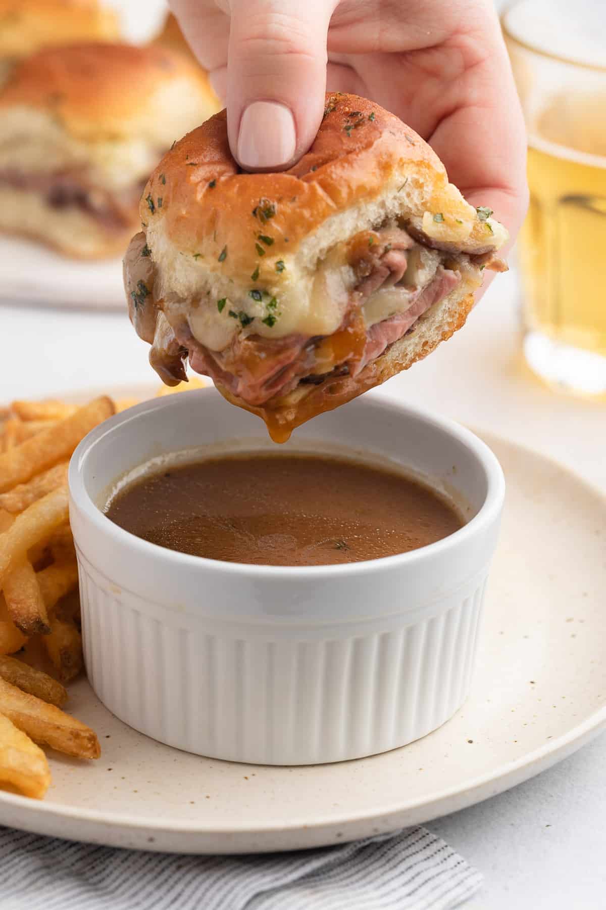 roast beef slider being dipped into a white ramekin of jus