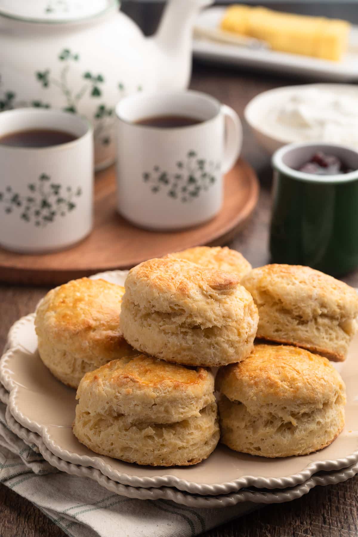Irish Scones on an ivory plate, with a tea set in the background and bowls of whipped cream and jam