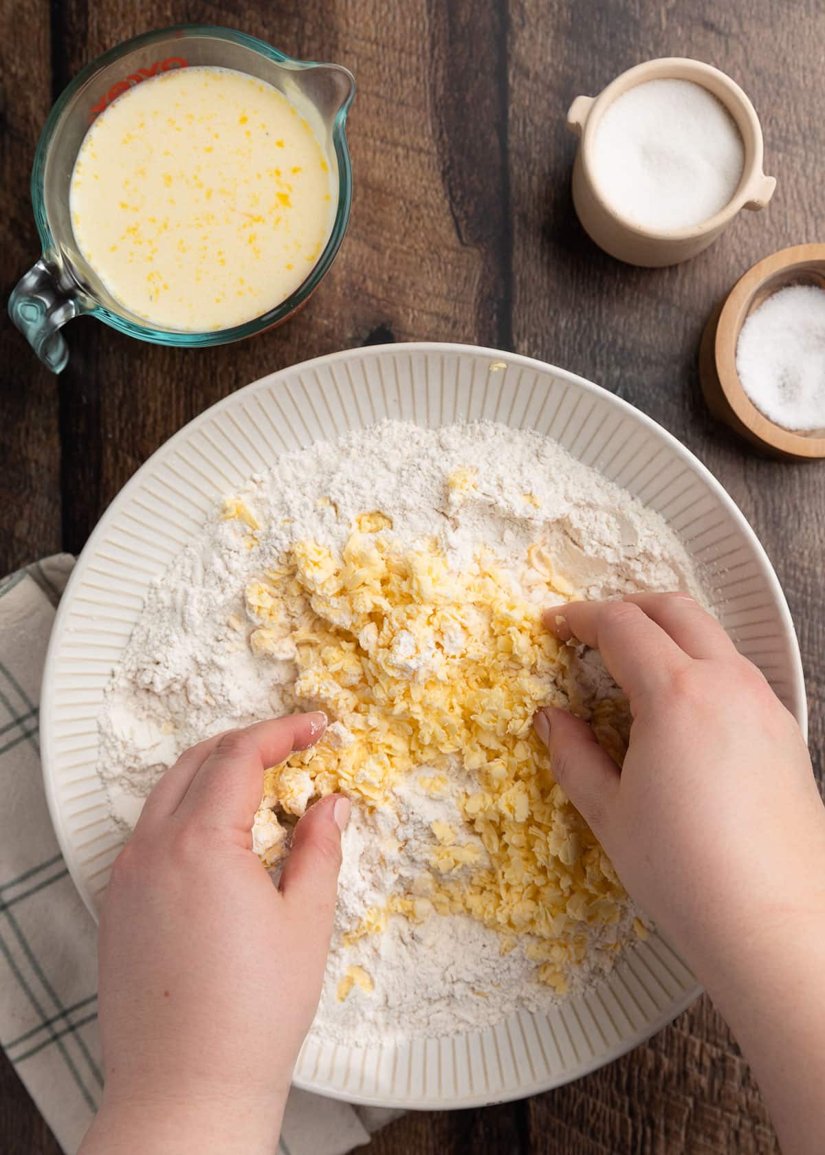 overhead photo of grated butter being incorporated into a bowl of dry ingredients by hand