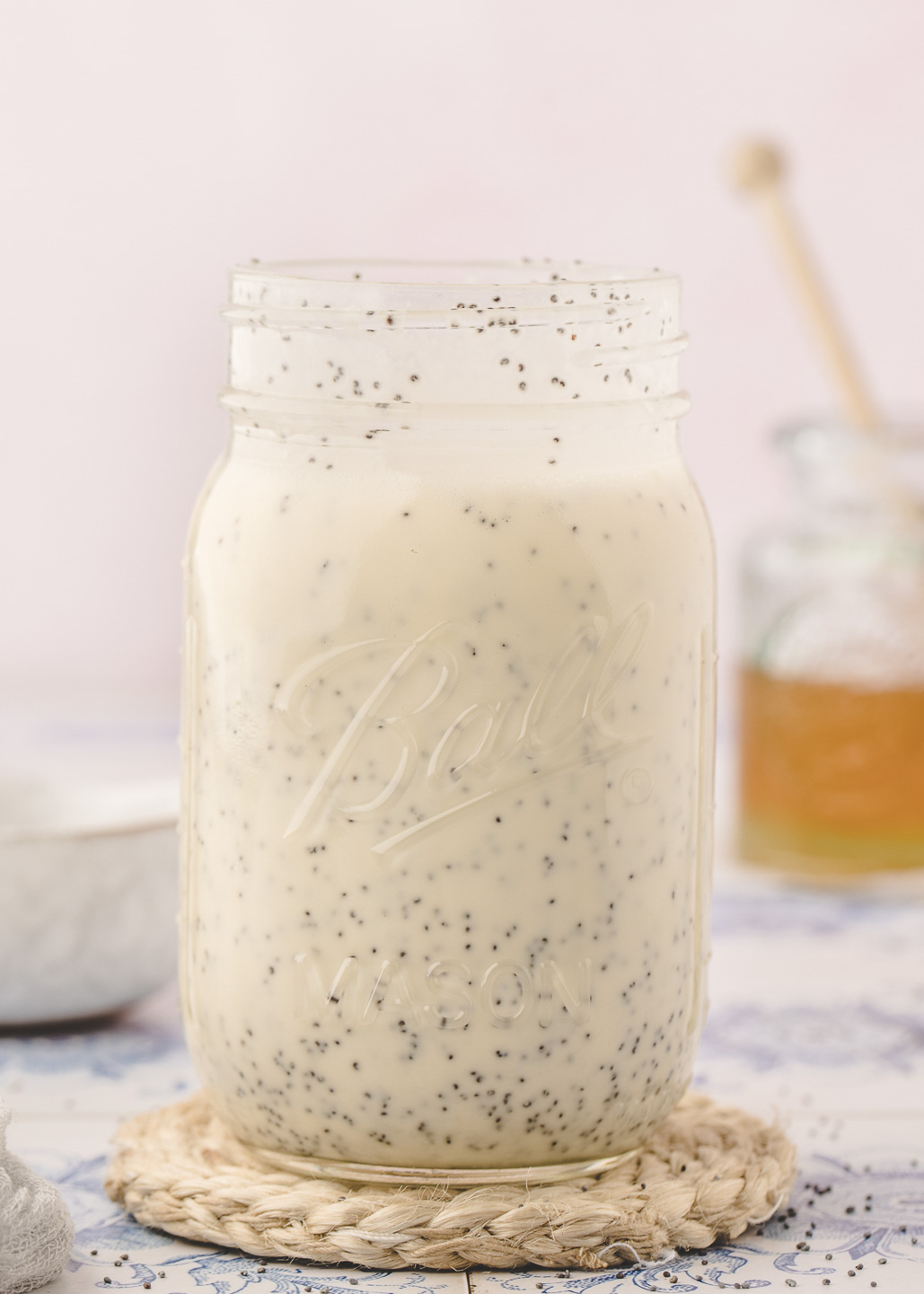 creamy poppyseed dressing in a ball mason jar in front of a jar of honey with a wooden dipper