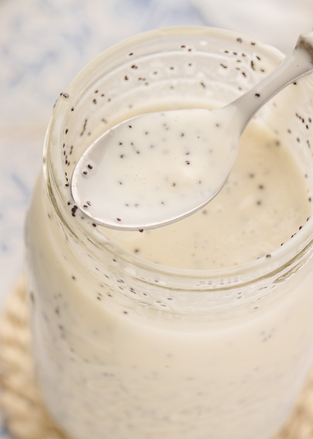 a mason jar of creamy poppy seed dressing with a spoonful of the dressing being held at the mouth of the jar
